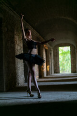 A ballerina performs in a black tutu, dancing gracefully in the dark room