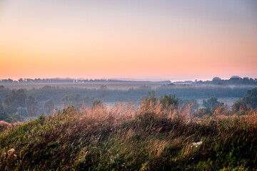 Red sunrise over the field with trees and forest . Morning at summer . Fog over the field and trees . Beautiful landsapes . Red sky and blue hour on nature . Smoothly foggy morning 