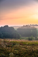 Red sunrise over the field with trees and forest . Morning at summer . Fog over the field and trees . Beautiful landsapes . Red sky and blue hour on nature . Smoothly foggy morning 