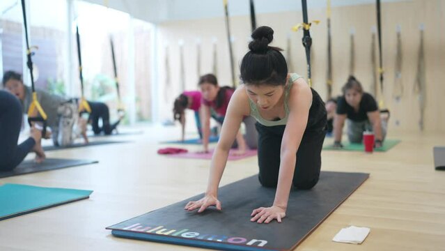 A group of women are doing yoga on mats with the word Lululemon on them. Scene is energetic and focused on physical fitness