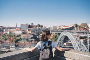 Young tourist enjoying beautiful landscape view in the old town with river and famous iron bridge during sunset in Porto city, Portugal.