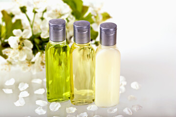 Three small bottles of cosmetics and flowers with leaves on white background, symbolizing naturalness and health. Shampoo, shower gel, body lotion. Travels, trips, hotels. Natural organic cosmetics