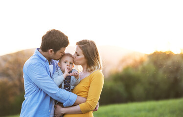 New parents holding small toddler, baby, outdoors in spring nature. Happy family moment