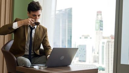 Businessman sitting on furniture working on laptop at ornamented corporate waiting area with...