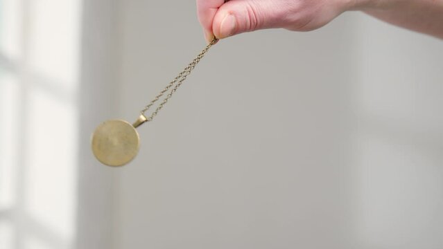 hypnosis session pendant on chain sways in female hand of hypnotist close-up.