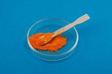 Tartrazine powder in Petri dish on blue background. Food coloring, pigment. Food additive E102....