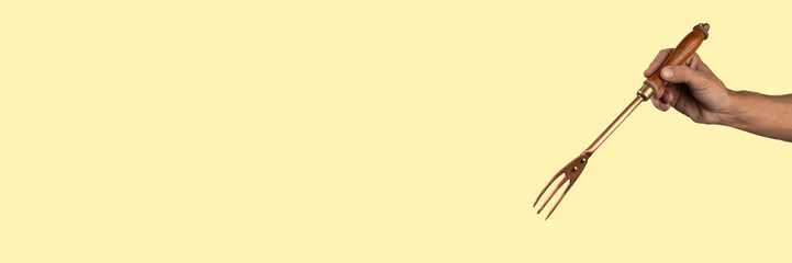 Black male hand holding a vintage brass meat fork on yellow banner