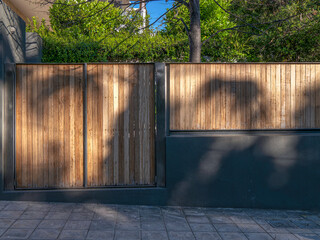 A contemporary design house fence entrance with a wooden pedestrian and car doors.Travel to Athens,...