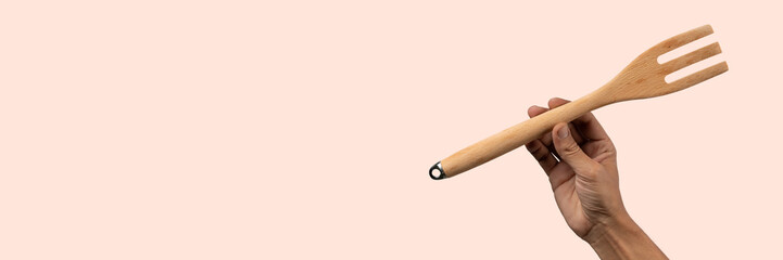Hand holding wooden cooking fork on pink banner background