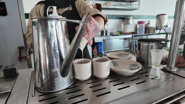An Indonesian woman making cup of hot coffee for customers breakfast in traditional coffee shop Kopi Tiam.
