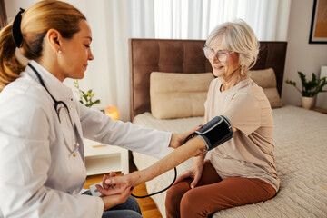 Family doctor is measuring senior woman's blood pressure at home during her visit and checkup.