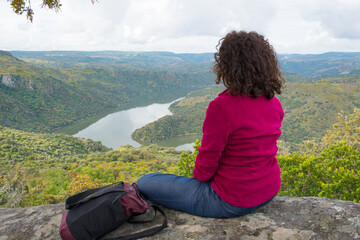 Rear view of woman sitting on mountain looking to beatiful landscape with river