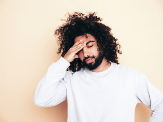 Handsome upset hipster model. Unshaven Arabian man dressed in summer clothes. Male with long curly hairstyle isolated on white in studio. with head in hand. Tired