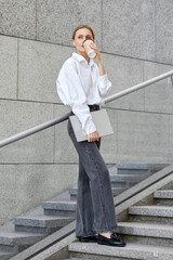 Portrait of a stylish young business lady dressed in a white shirt walking around the city during...