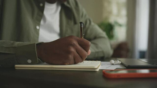 Close up of man's hand writing with pen in notebook