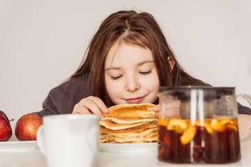 Little girl of pre-adolescence, inhales the aroma of freshly baked pancakes stacked in a stack....
