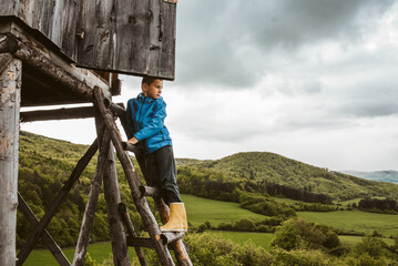 Boy on ladder of hunting blind during their walk in forest, climbing up to observe beautiful spring...