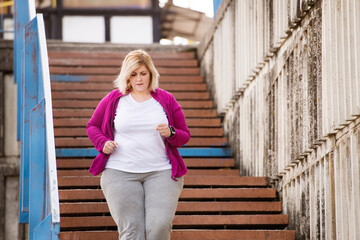 Overweight woman running in city, down the stairs. Exercising outdoors for people with obesity.