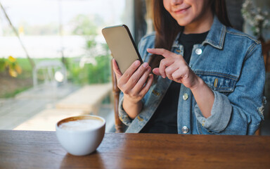 Closeup image of a woman holding and using mobile phone in cafe