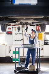 Female auto mechanic elevating car on car lift, changing oil. Beautiful woman working in a garage,...