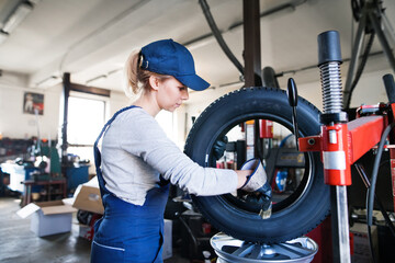 Female auto mechanic changing tieres in auto service. Beautiful woman holding tire in a garage,...