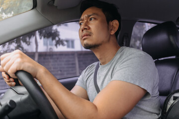 Side view of unhappy face of asian man who driving a car on road while traveling alone, going to work, bad traffic jam.