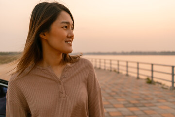 Photo of asian woman smiling and standing next to the river at sunset time, chilling traveling on vocation