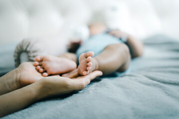 Mom hands holding baby feet lying on a comfortable bed at home,Newborn child
