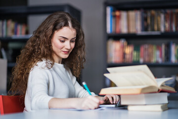 Young female student in library, focusing on final project, presentation. University student preparing for final exam.