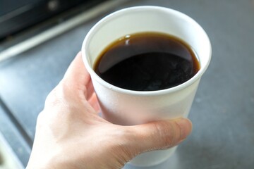 紙コップに注いだコーヒーを持つ人の手元アップ