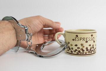 A man in handcuffs is combined with a cup of coffee. The concept of coffee addiction.