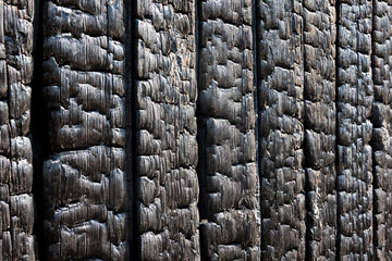 A perspective view of a burnt wall of a wooden house. Black boards covered with charcoal. Background. Texture. Abstraction.