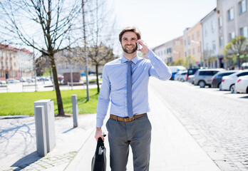 Handsome businessman phone calling on smartphone, standing in city street. Working remotely,...