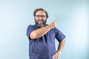 Fototapeta premium Horizontal banner of smiling young male doctor showing and presenting something with hand, isolated on blue background with copy space on right