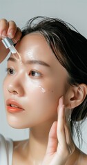 A close-up shot of an Asian woman's face, applying serum with a dropper bottle to her cheek against a white background. 