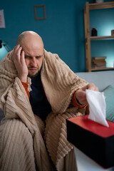 bearded sick man on couch at home suffers from runny nose, sneezes. Unwell guy taking napkin...