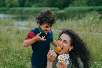 Heartwarming moment of a mother and son enjoying nature, with the son playfully interacting as his mother bites into an apricot