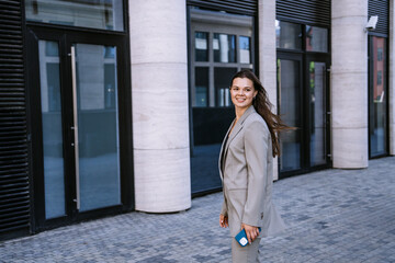 Confident young businesswoman walking outside modern office buildings, looking poised and professional in a stylish suit