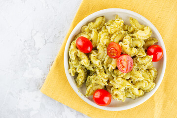 Pasta Creste Di Gallo with cherry tomatoes and pesto sauce in a plate on a table. Top view.