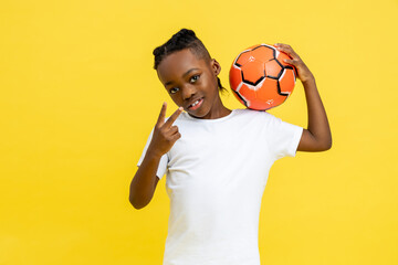 Afro-American little boy wearing white T-shirt posing with ball showing victory sign