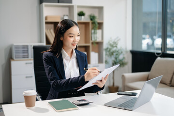  Asian woman using laptop and tablet while sitting at her working place. Concentrated at work.