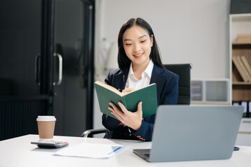  Asian woman using laptop and tablet while sitting at her working place. Concentrated at work.