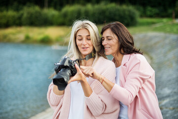 Adult daughter teaching mother how to take photos with professional camera, explaining technology, laughing. Mother's Day concept.