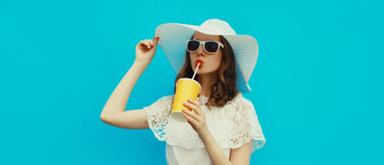 Summer portrait of beautiful young woman with cup of fresh juice wearing hat on blue background