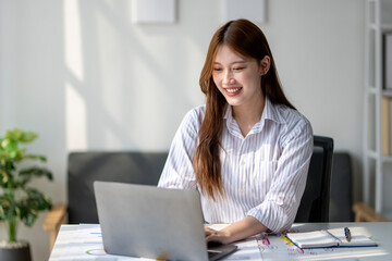 A woman is sitting at a desk with a laptop in front of her. She is smiling and she is enjoying her work