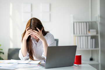 A woman is sitting at a desk with a laptop and a red cup. She is looking at the laptop with a worried expression on her face