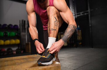 Handsome muscular man tying shoelaces on sneakers in gym. Routine workout for physical and mental health.