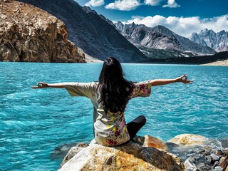 Girl with Open Arms Sitting on Rock and Enjoying Beautiful Mountains with Lake