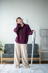 A woman in a purple sweater and tan pants is standing in front of a white vacuum cleaner. She is...