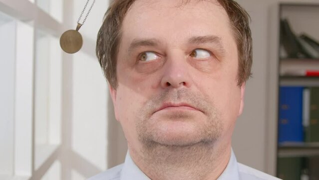 Man in hypnosis session with his eyes follows swinging hypnotic pendant on chain in front of face.
